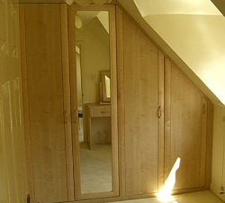 Bespoke fitted wardrobes for a sloping ceiling with Maple doors and matching dressing unit with chamfered design. 