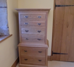 Solid Wood Tall Boy incorporating laundry bin. This piece was commissioned as part of a bedroom set: a four poster bed, wardrobes & two bedside drawer units. This solid Oak tall boy incorporates a laundry bin, hidden behind false drawer fronts in the base of the unit. Four drawers form the top of the unit built with dovetailed joints & soft close drawer runners.