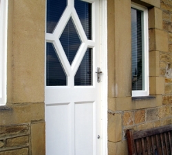 A hand painted, softwood door featuring a bespoke diamond shaped central window.