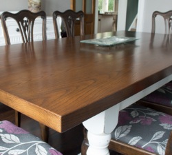 Solid Oak table top stained dark to match the existing chairs with turned legs - painted white and distressed to create a shabby chic farmhouse dining table.