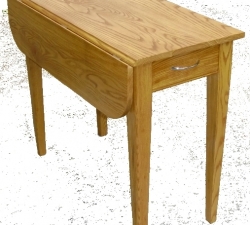 This is a small drop leaf table built in solid Ash. The table was built to fit into a small space in a kitchen and seats two people when the drop leaf is being used. The table also incorporates a cutlery drawer with dove tailed joints and features tapered legs. Stained to match the clients existing Beech chairs.